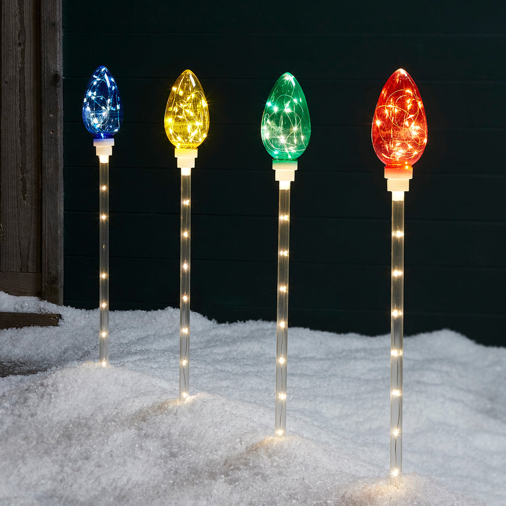 Vier bunte Stableuchten in Blau, Gelb, Grün und Rot mit Lichterkette im Schnee bei Nacht