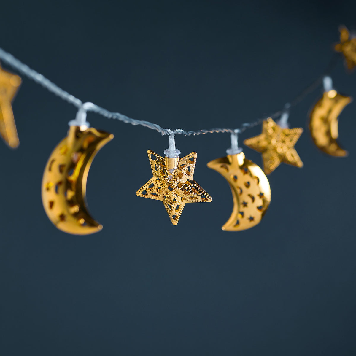 Nahaufnahme goldener Metallsterne und Monde der Lichterkette mit warmweißen LEDs an transparentem Kabel