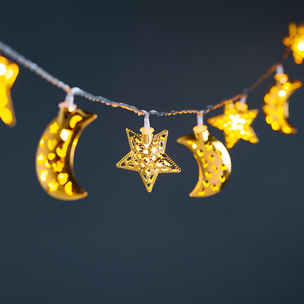 Goldene Lichterkette mit leuchtenden Metallsternen und Monden an transparentem Kabel vor dunklem Hintergrund