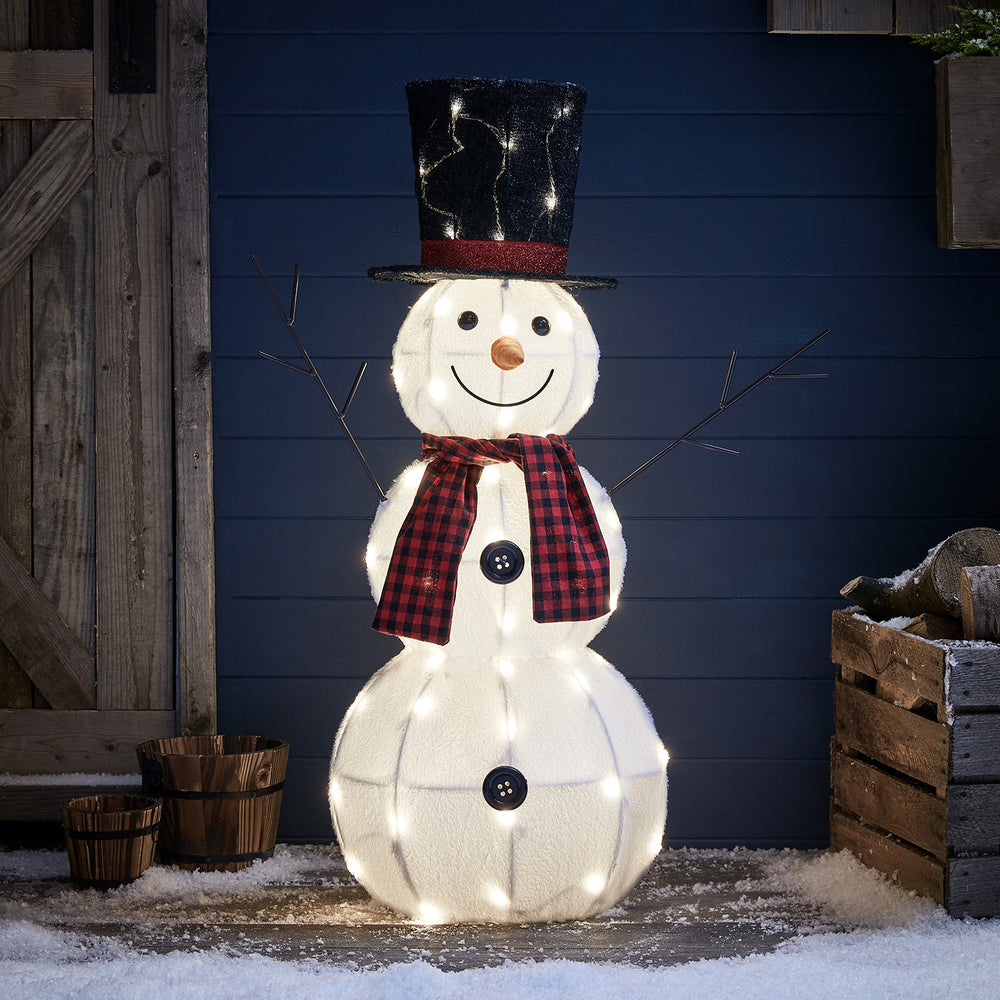 Beleuchteter LED Schneemann mit schwarzem Zylinderhut und rot-schwarzem Schal vor dunkler Wand im Außenbereich