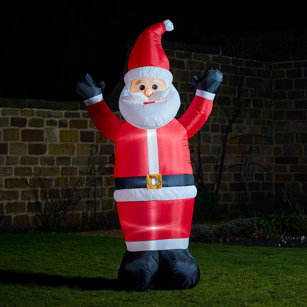Aufblasbarer Weihnachtsmann mit rotem Mantel und Mütze winkt im Garten bei Nacht