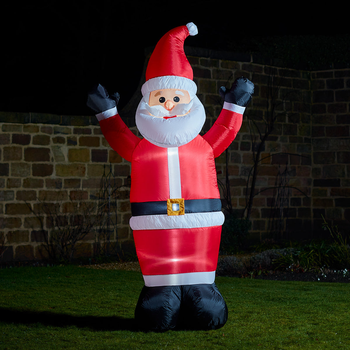 Aufblasbarer Weihnachtsmann mit rotem Mantel und Mütze winkt im Garten bei Nacht
