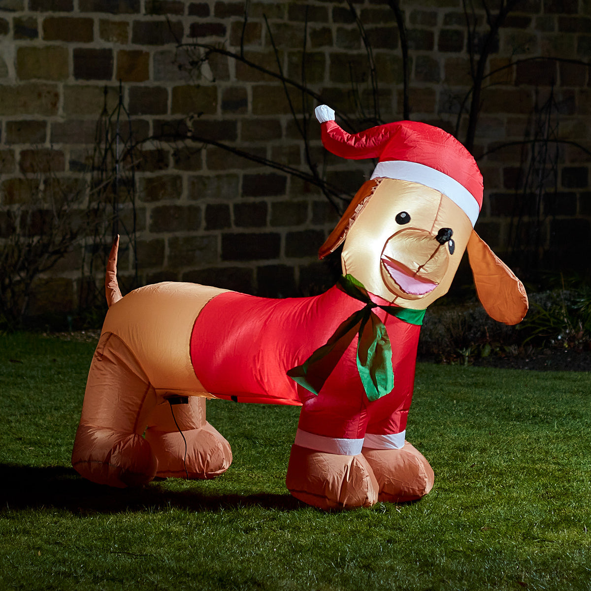 Aufblasbare LED Weihnachtsfigur in Form eines Dackels mit rotem Weihnachtsmütze und grünem Schal im Garten