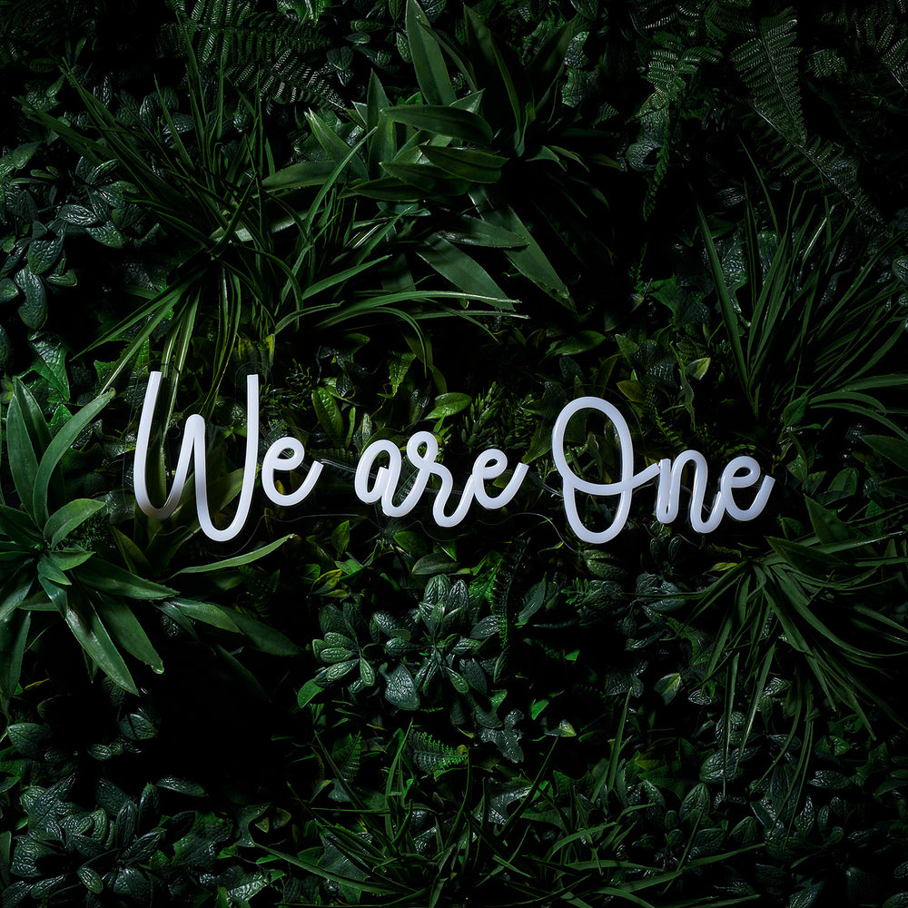 LED Neon Schriftzug We are One in Weiß ohne Beleuchtung vor Pflanzen