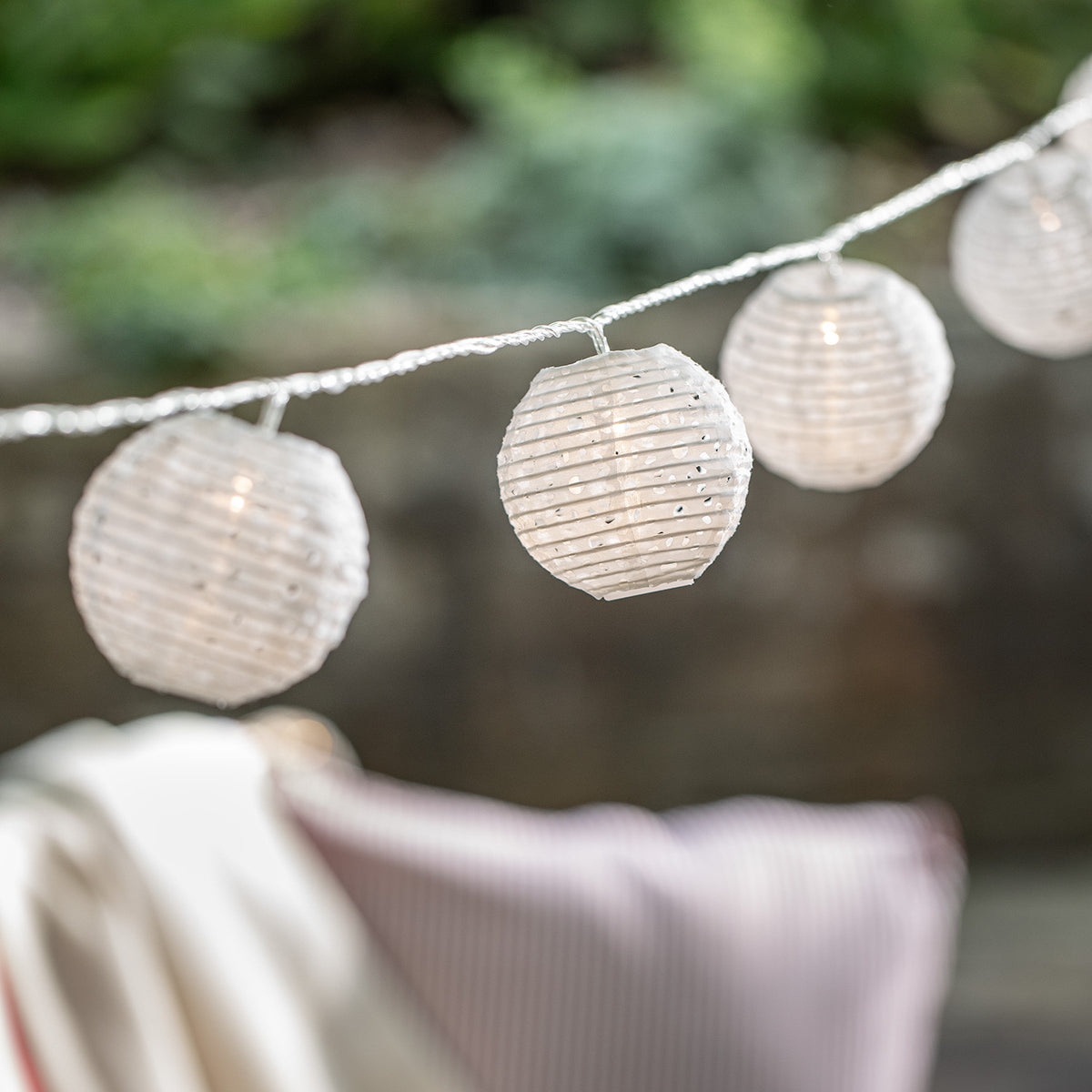 Nahaufnahme von weißen Lampions mit Cut-Out Muster an einer Lichterkette im Garten