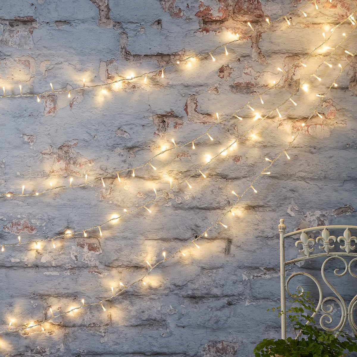 Bicolor LED Lichterkette warmweiß an alter Backsteinwand drapiert mit Metallstuhl