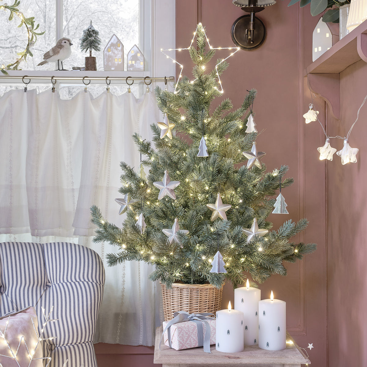 Weihnachtsbaum mit Sternen- und Tannenbaum-Anhängern auf Holztisch neben Kerzen und Geschenk im Wohnzimmer