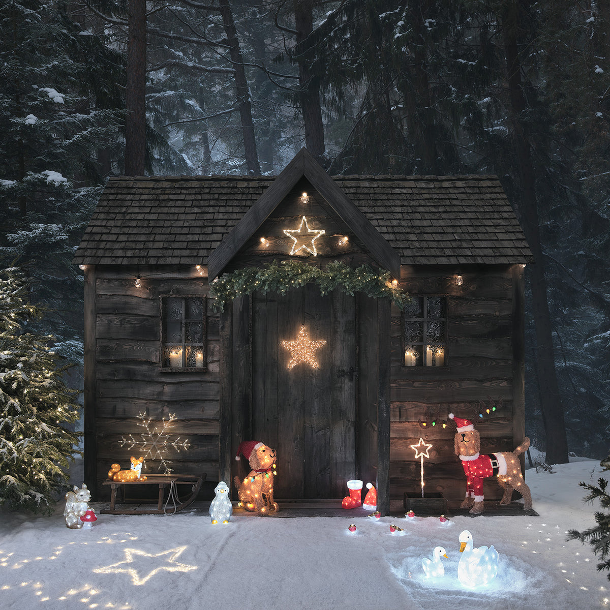 Weihnachtliche Dekoration mit LED-Welpenfigur, Stern und weiteren Figuren vor Holzhütte im Schnee