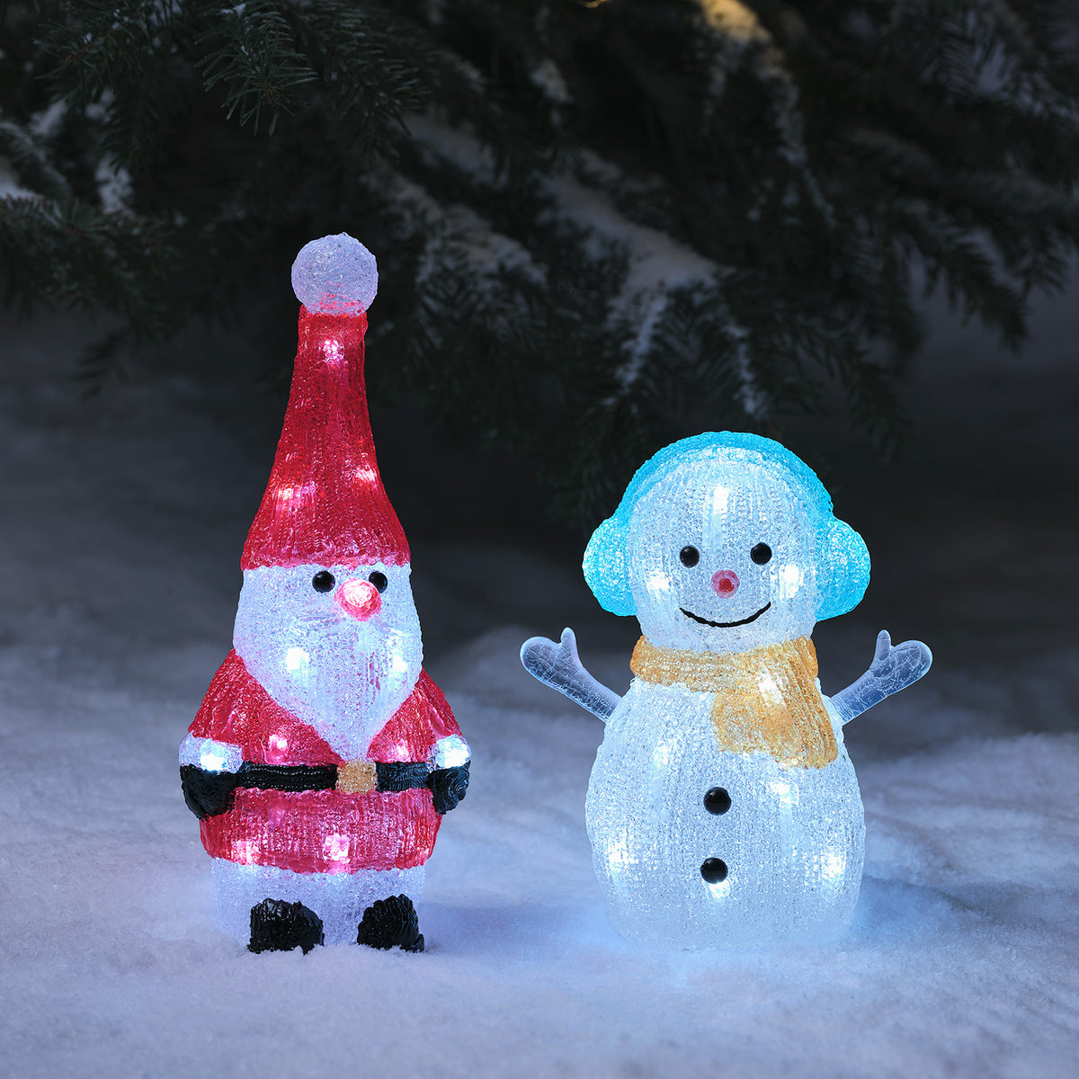 Leuchtender Acryl Weihnachtsmann neben beleuchtetem Schneemann mit blauen Ohrenschützern im Schnee