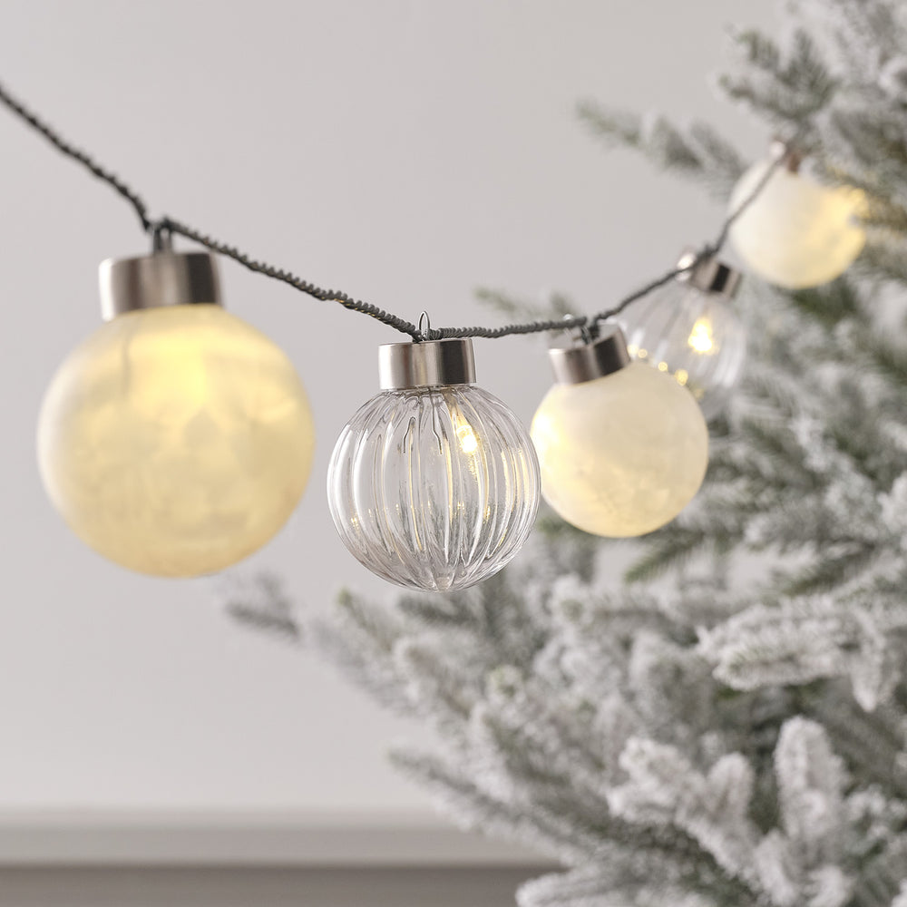Nahaufnahme LED Lichterkette mit warmweißen und klaren Weihnachtsbaumkugeln an grünem Kabel