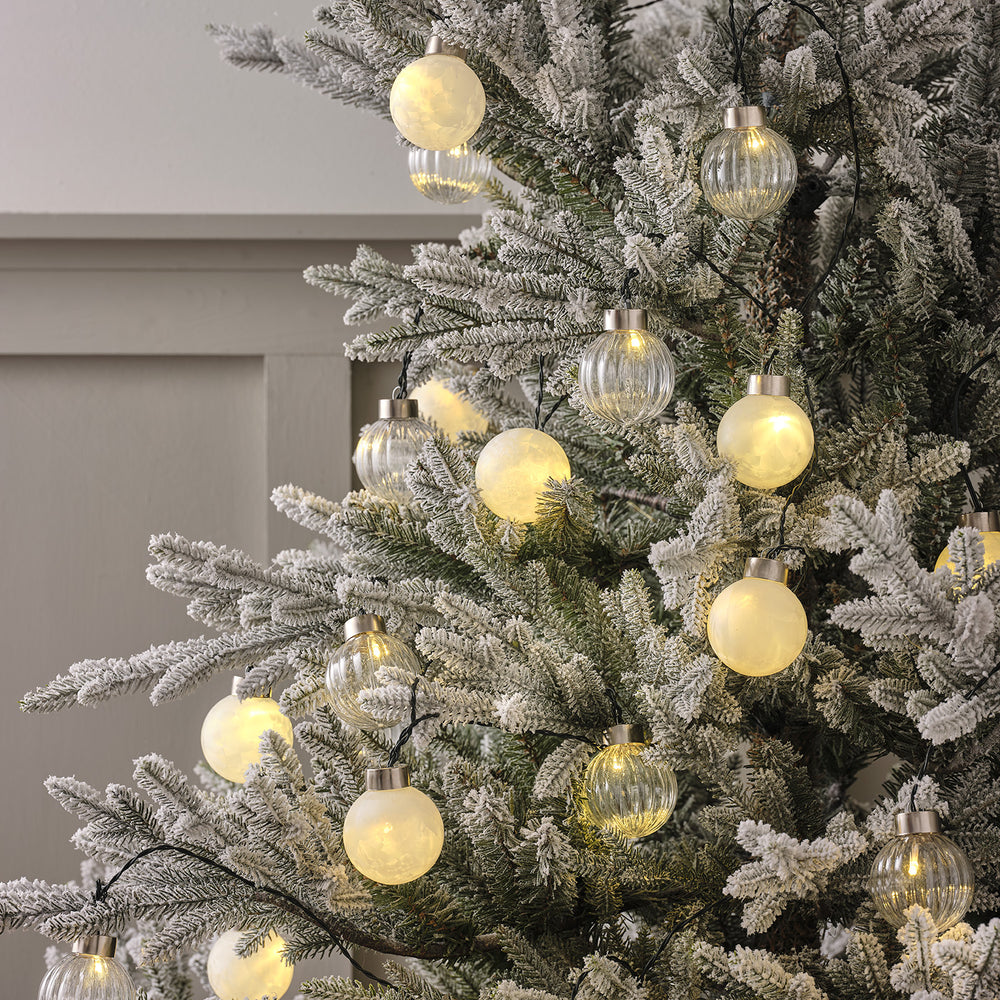 LED Lichterkette mit warmweißen und klaren Kugeln dekoriert an einem künstlichen Tannenbaum