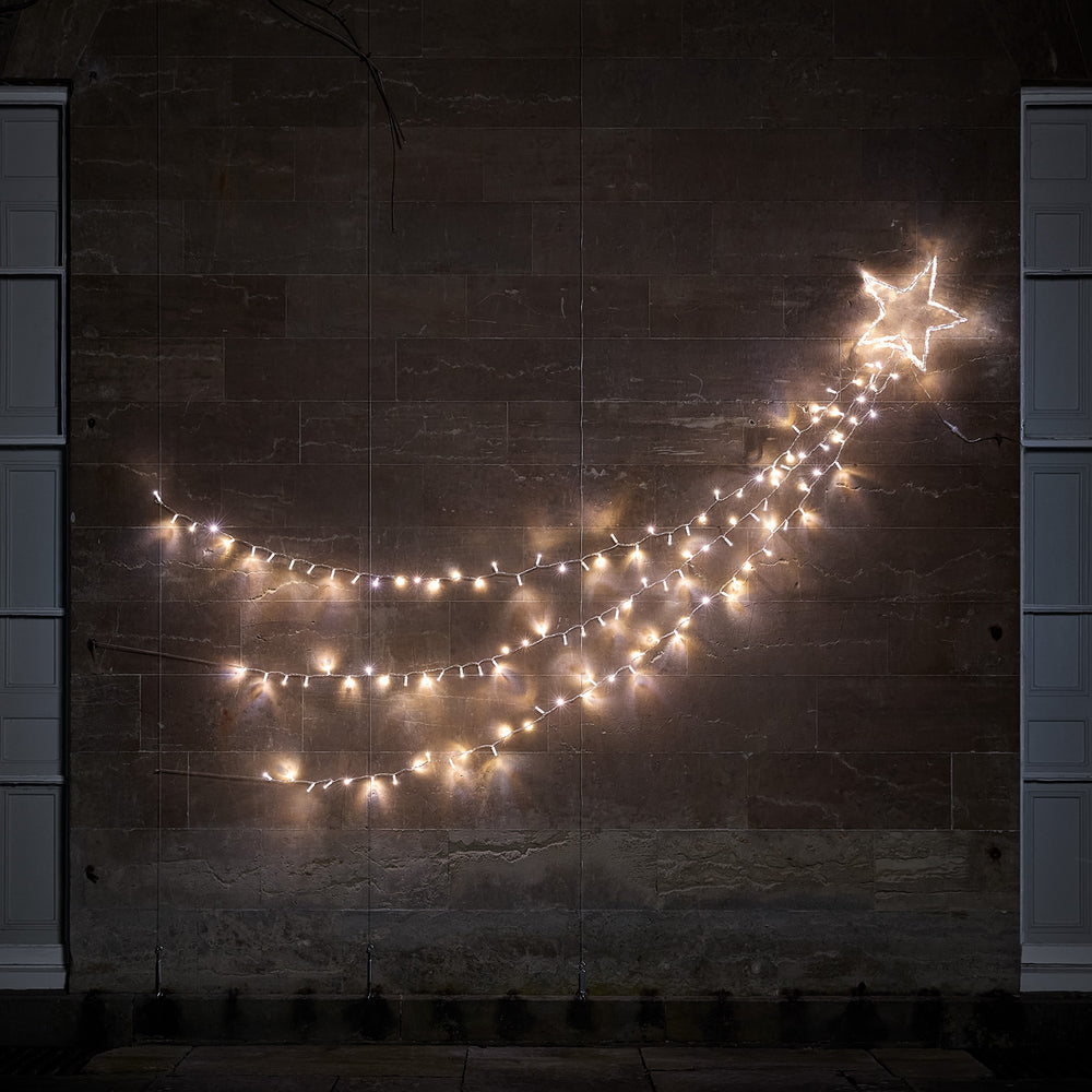 Bicolor LED Sternschnuppe mit weiß und warmweiß leuchtenden Lichtsträngen an dunkler Wand