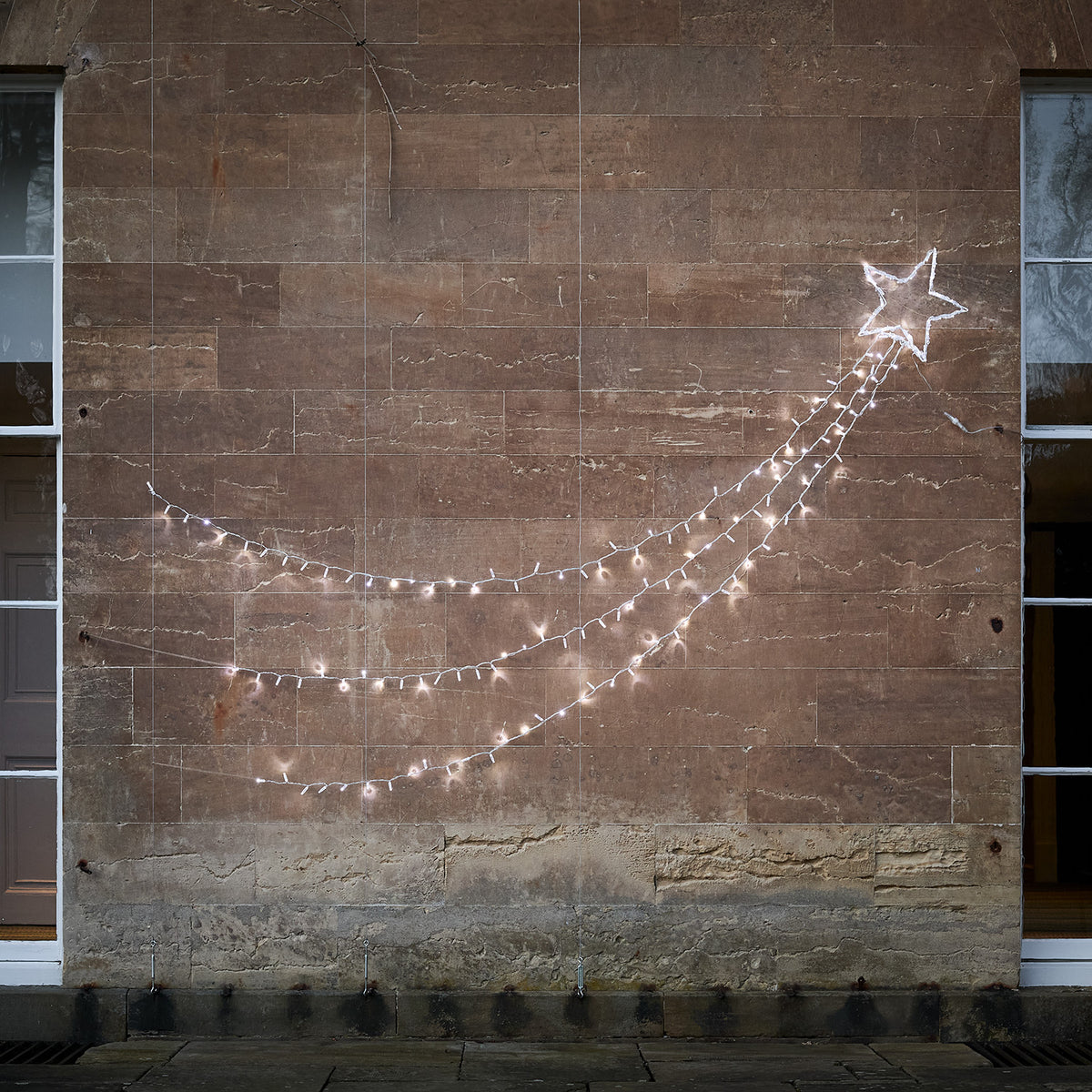 Bicolor LED Sternschnuppe mit weiß und warmweiß leuchtenden Lichtsträngen an heller Wand