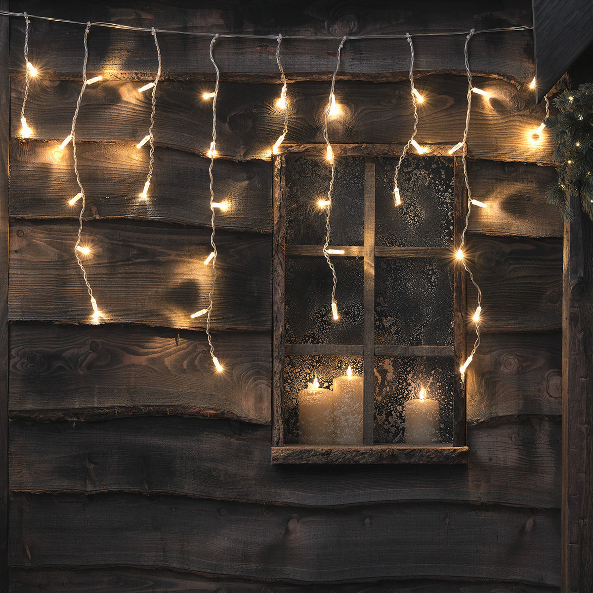 Bicolor LED Eiszapfen Lichterkette in warmweiß an Holzwand mit Fenster und Kerzen