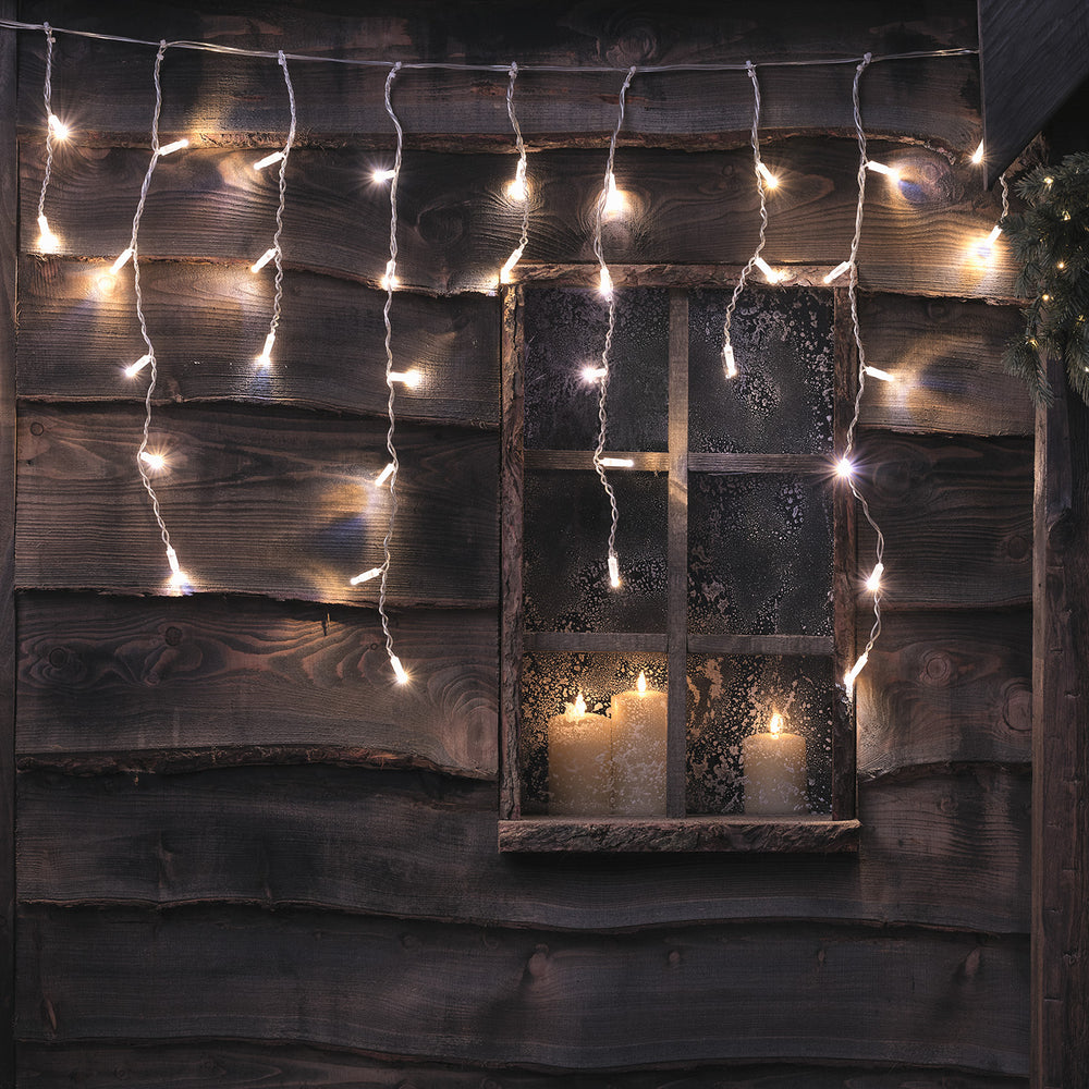 Bicolor LED Eiszapfen Lichterkette in weiß an Holzwand mit Fenster und Kerzen