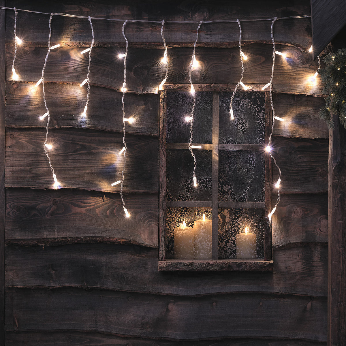Bicolor LED Eiszapfen Lichterkette in weiß an Holzwand mit Fenster und Kerzen