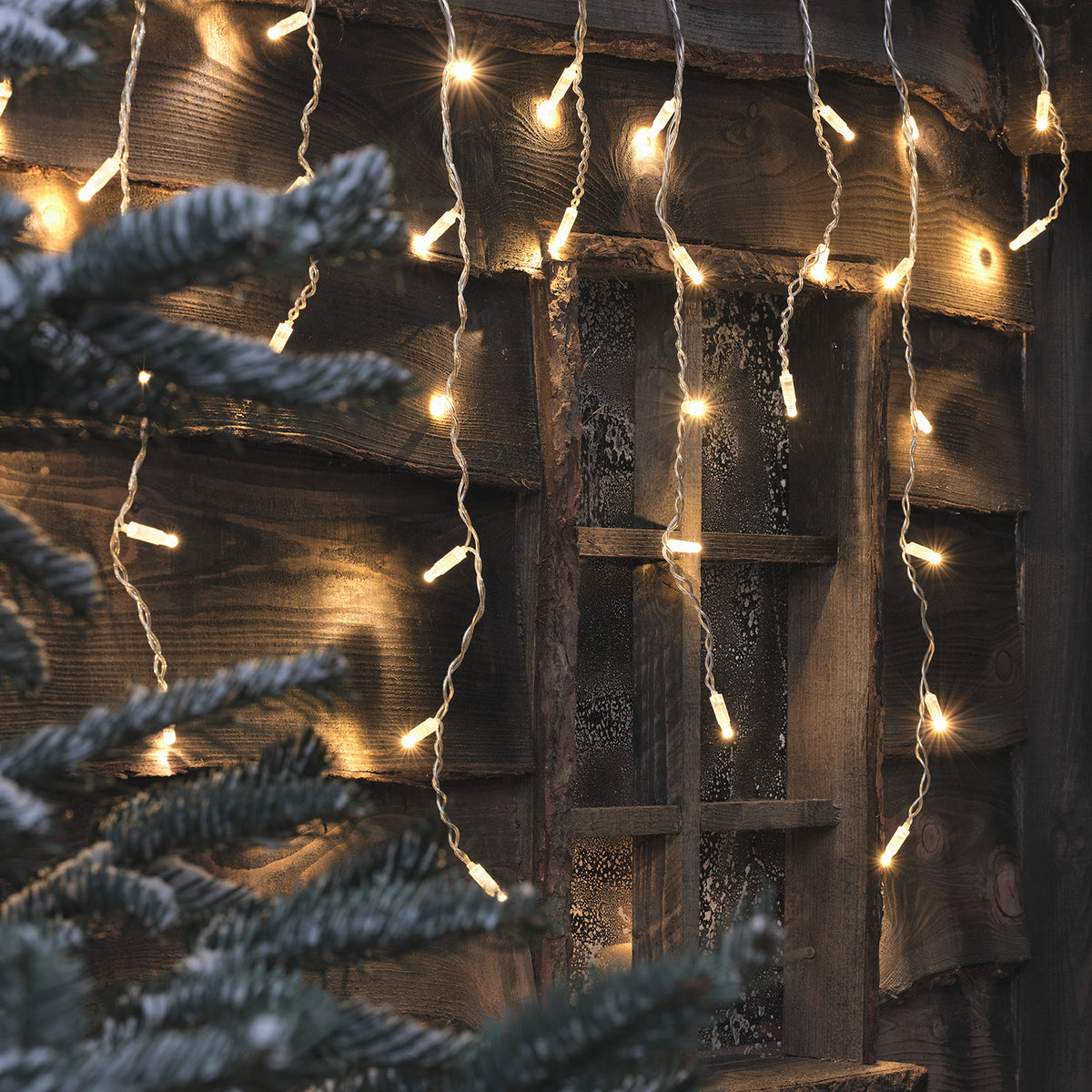 Nahaufnahme der weißen Bicolor LED Eiszapfen Lichterkette an Holzwand mit Fenster