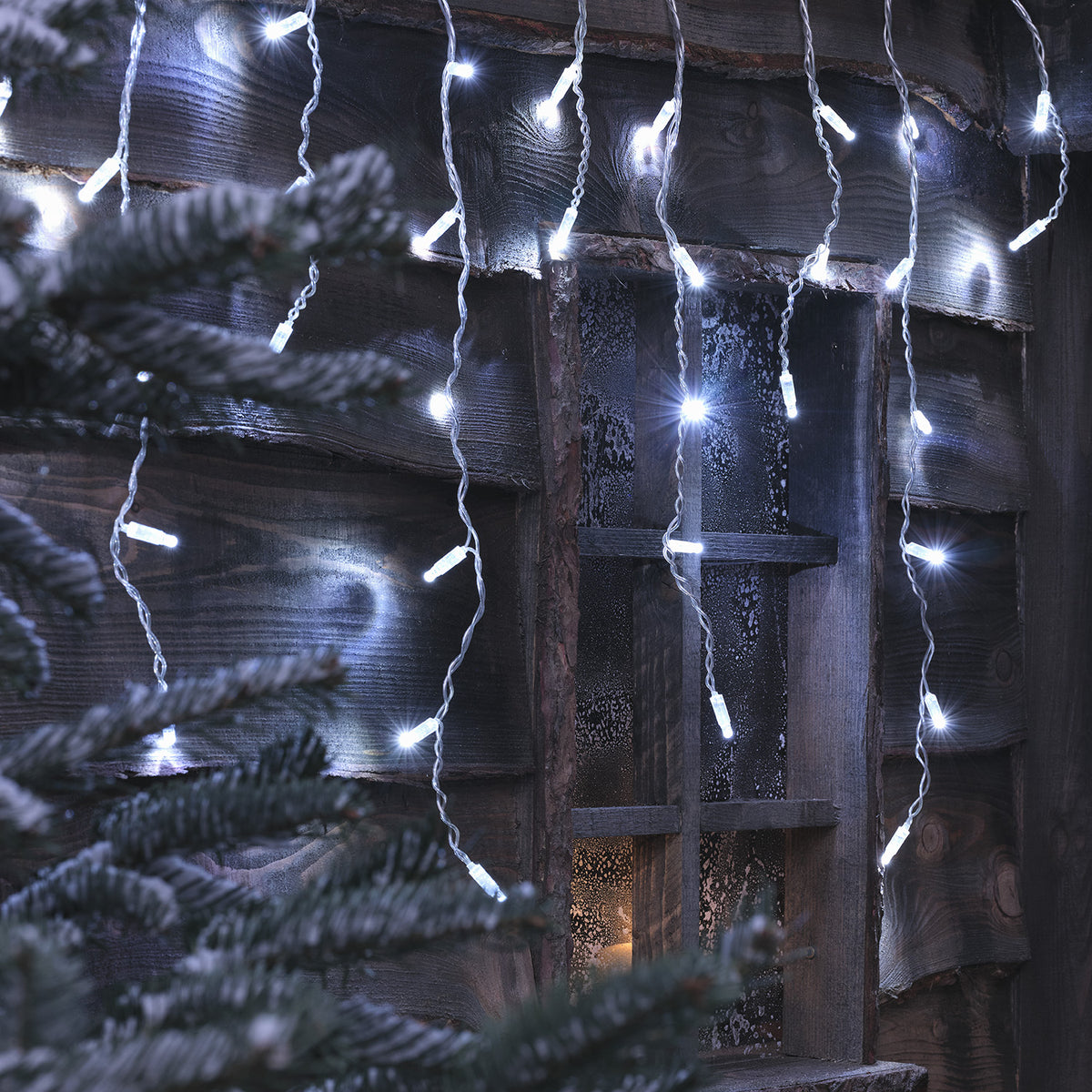 Nahaufnahme der kaltweißen Bicolor LED Eiszapfen Lichterkette an Holzwand mit Fenster