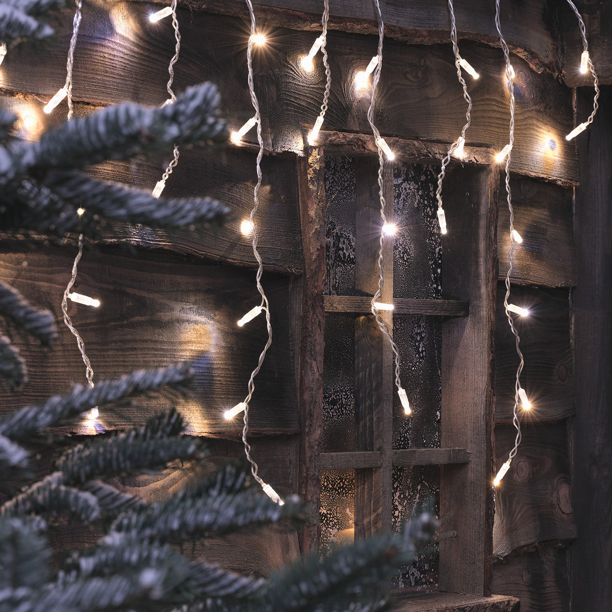 Nahaufnahme der warmweißen Bicolor LED Eiszapfen Lichterkette an Holzwand mit Fenster