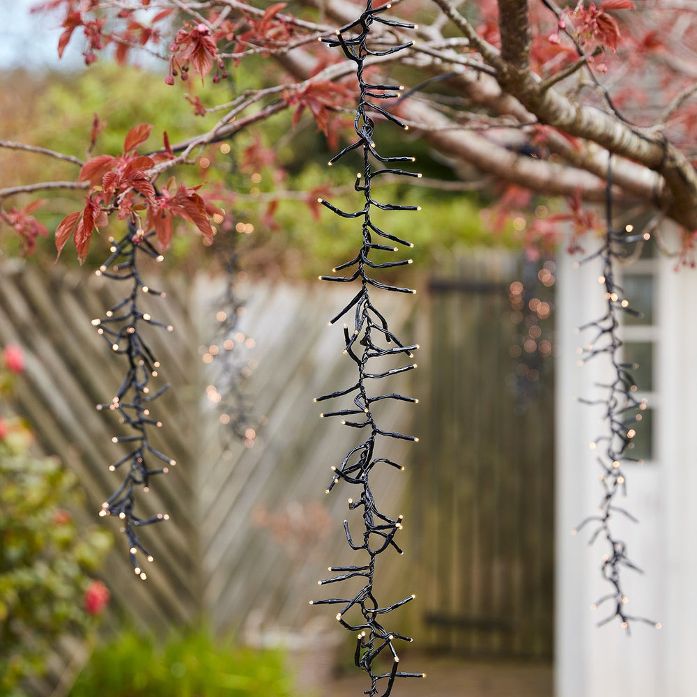 Unbeleuchtete LED-Kaskadenlichter hängen an Ästen eines Baumes im Garten bei Tageslicht