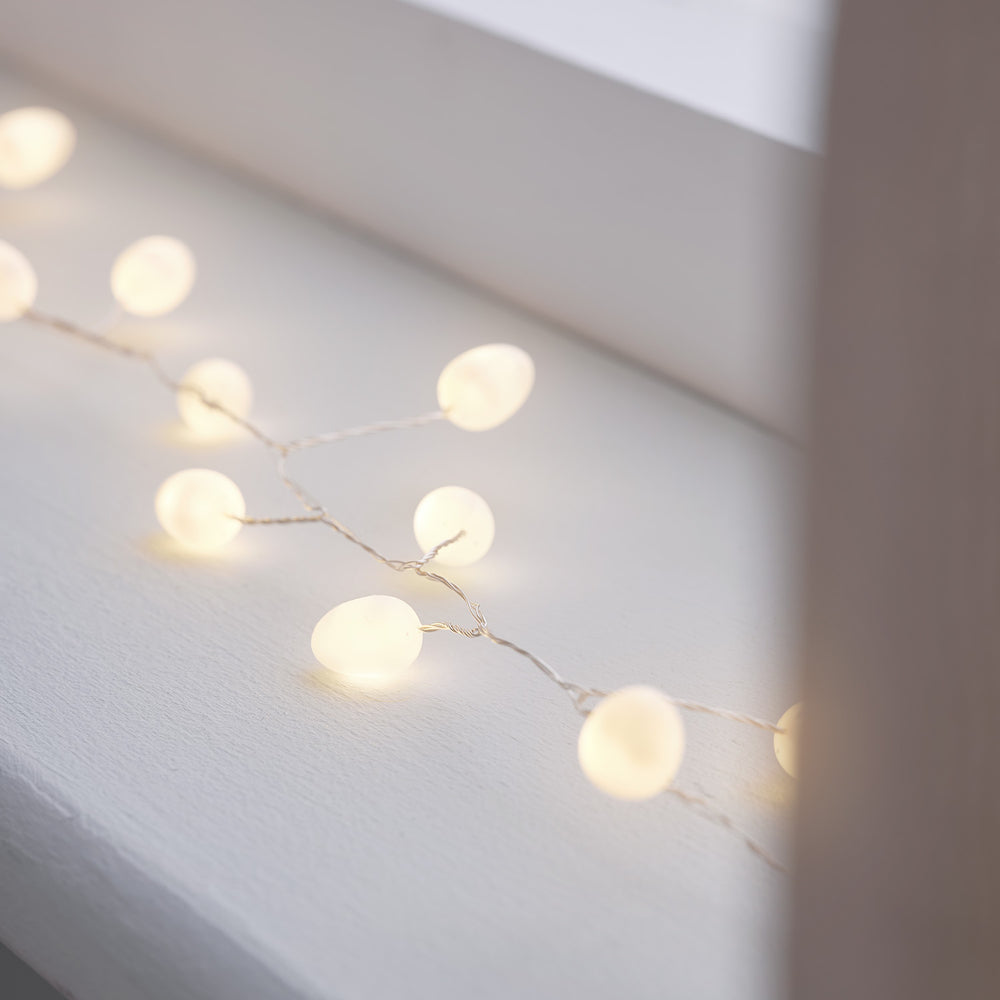 Nahaufnahme der Lichterkette mit weißen Beeren und warmweißen LEDs auf weißem Untergrund