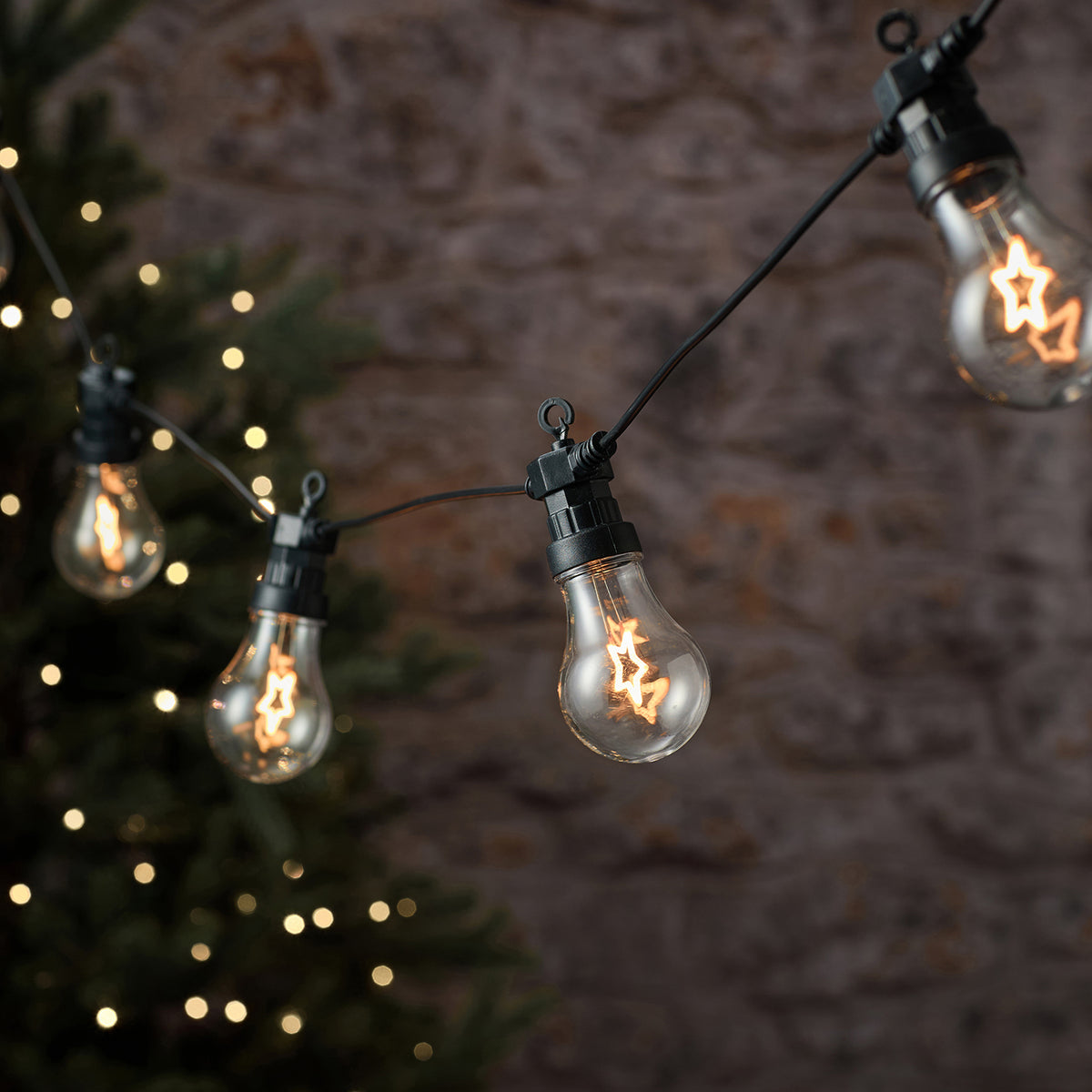 LED-Lichterkette mit zehn warmweißen Stern-LEDs an schwarzem Kabel vor Steinwand