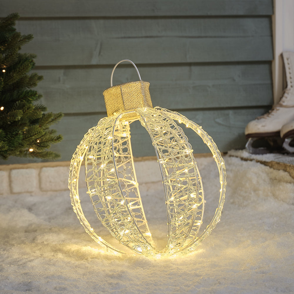 Nahaufnahme einer warmweißen LED-Weihnachtskugel mit goldfarbener Kappe und Haken im Schnee