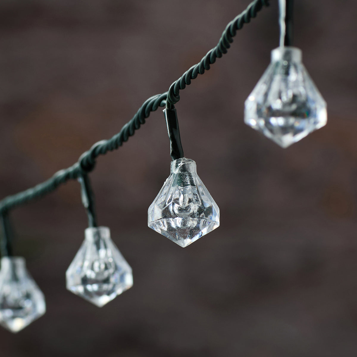 Detailaufnahme einer klaren facettierten Diamant-Kappe der LED-Lichterkette an grünem Kabel