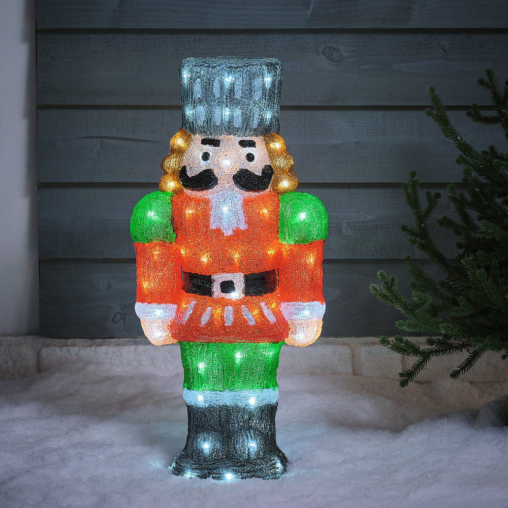 Beleuchteter LED-Nussknacker aus Acryl mit rotem Mantel und grünen Schulterklappen im Schnee