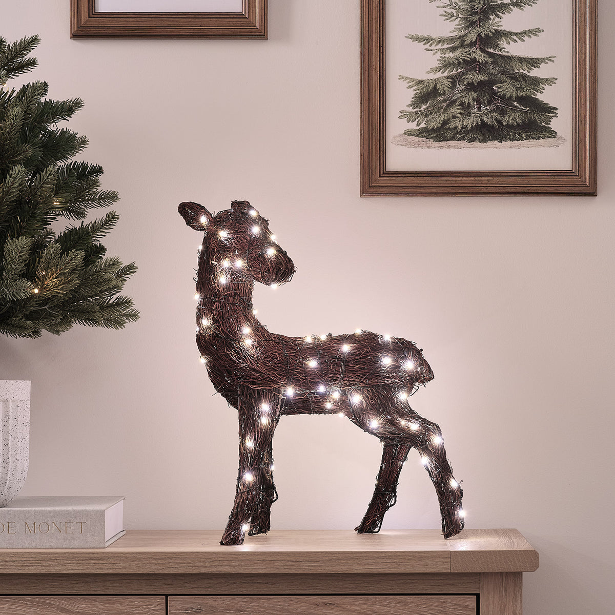 Bicolor LED-Hirschkuh in Zweigoptik mit warmweißem und weißem Licht auf Holzkommode neben Tannenzweig und Bilderrahmen