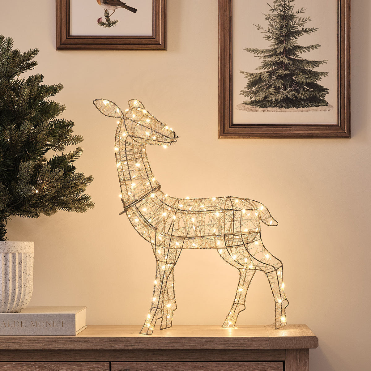Goldene LED-Rentier-Hirschkuh mit warmweißem Licht auf Sideboard vor Wand mit Bildern