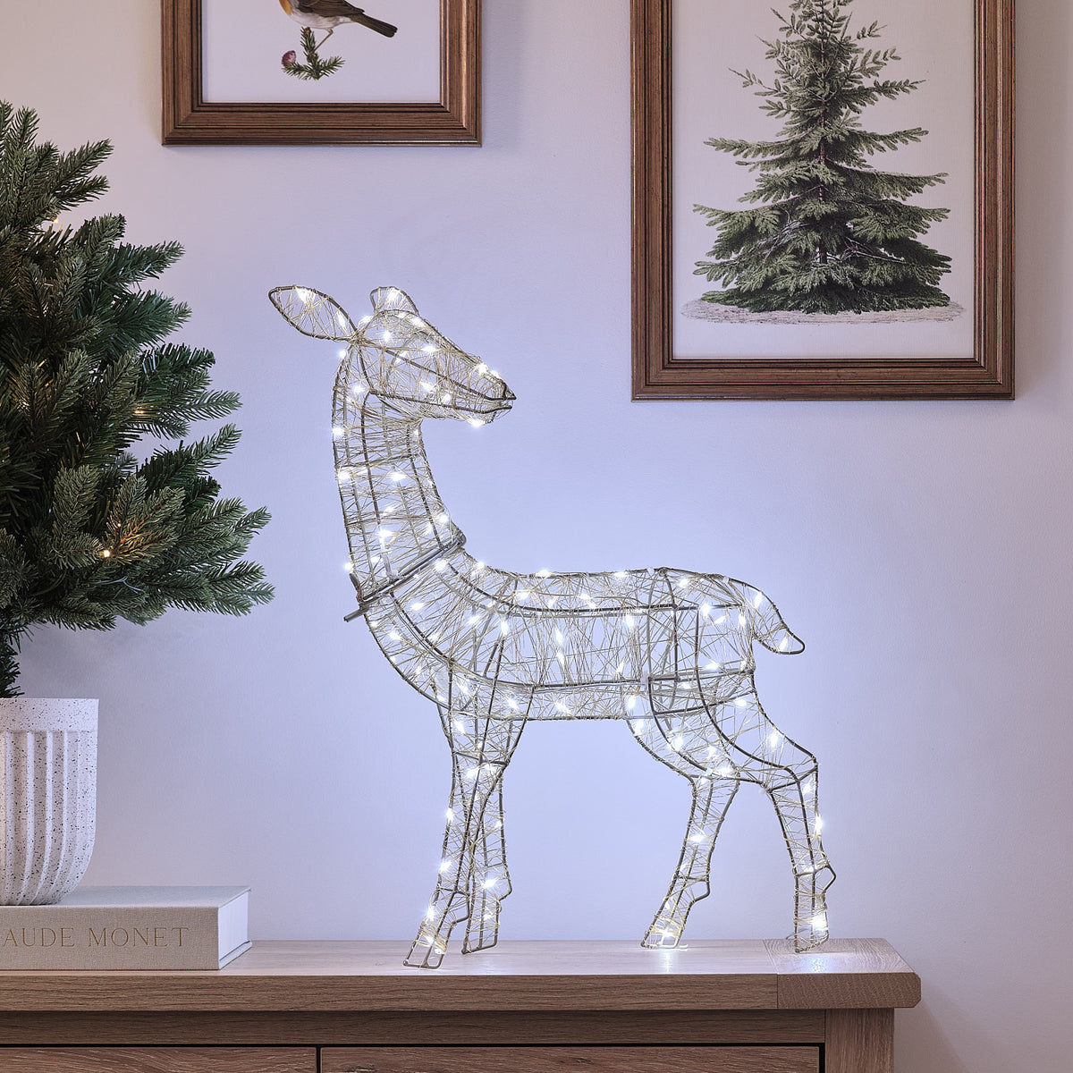 Goldenes LED-Rentier Hirschkuh mit weißen Mikro-LEDs auf Holzkommode neben Tannenzweig