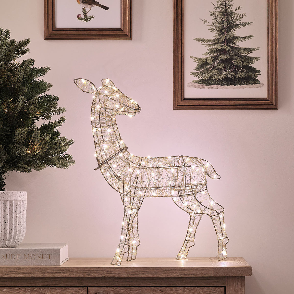 Goldene LED-Rentier-Hirschkuh mit warmweißem Licht auf Sideboard vor Wand mit Bildern