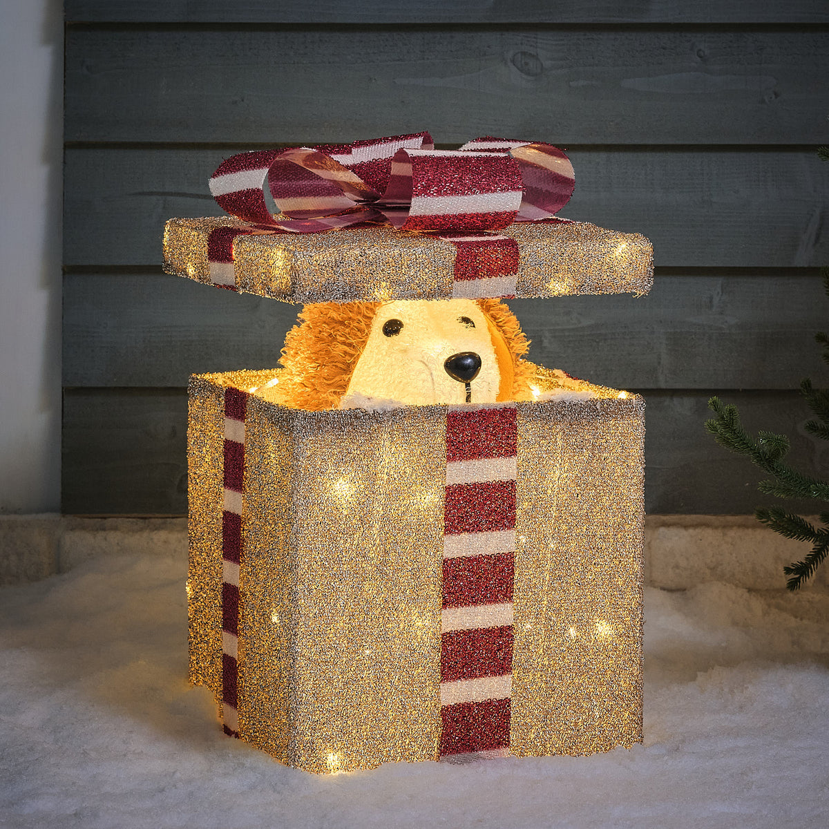 Leuchtende LED-Weihnachtsfigur Hund schaut aus glitzerndem Geschenk mit rotem Band