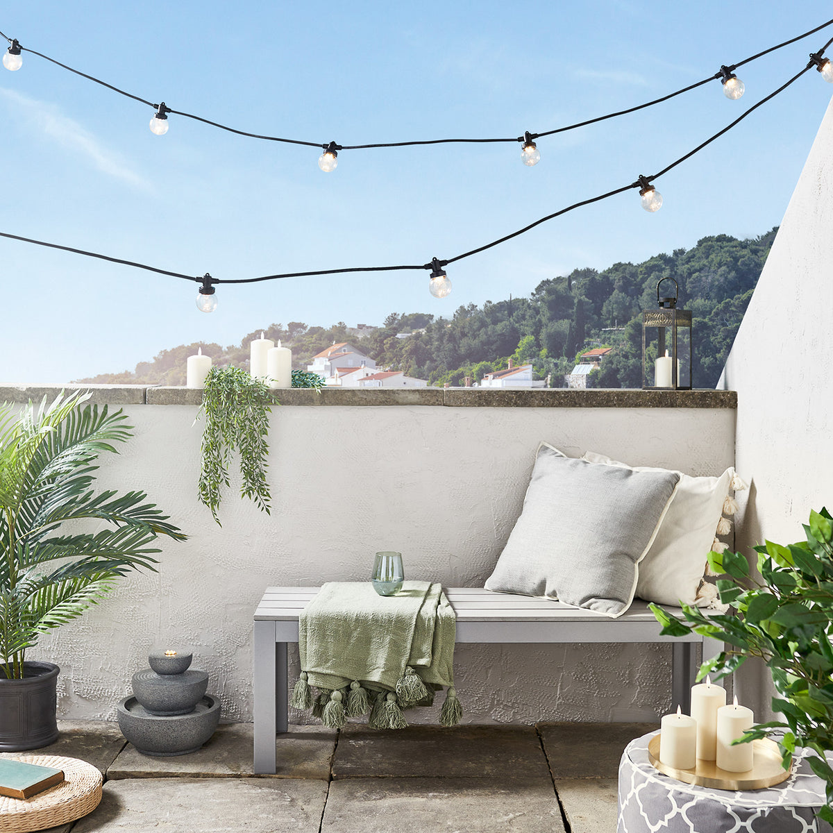 Zwei schwarze Lichterketten mit warmweißen Glühbirnen auf Balkon mit Sitzbank und Pflanzen