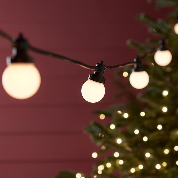 Warmweiße LED-Glühbirnen an schwarzem Kabel vor roter Wand und Weihnachtsbaumbeleuchtung