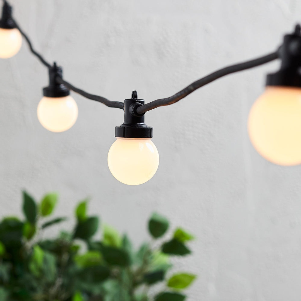 Nahaufnahme einer warmweißen LED-Glühbirne an schwarzem Kabel der Party Lichterkette