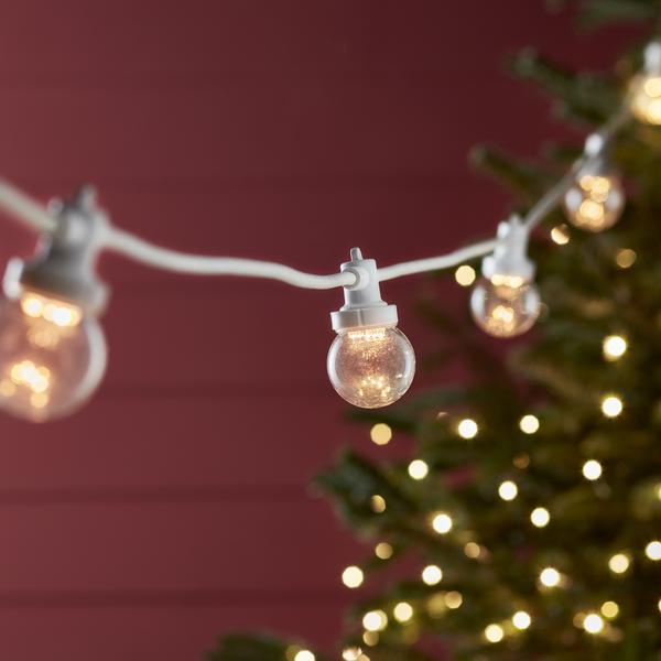 Warmweiße LED-Glühbirnen an weißem Kabel vor roter Wand und Weihnachtsbaum