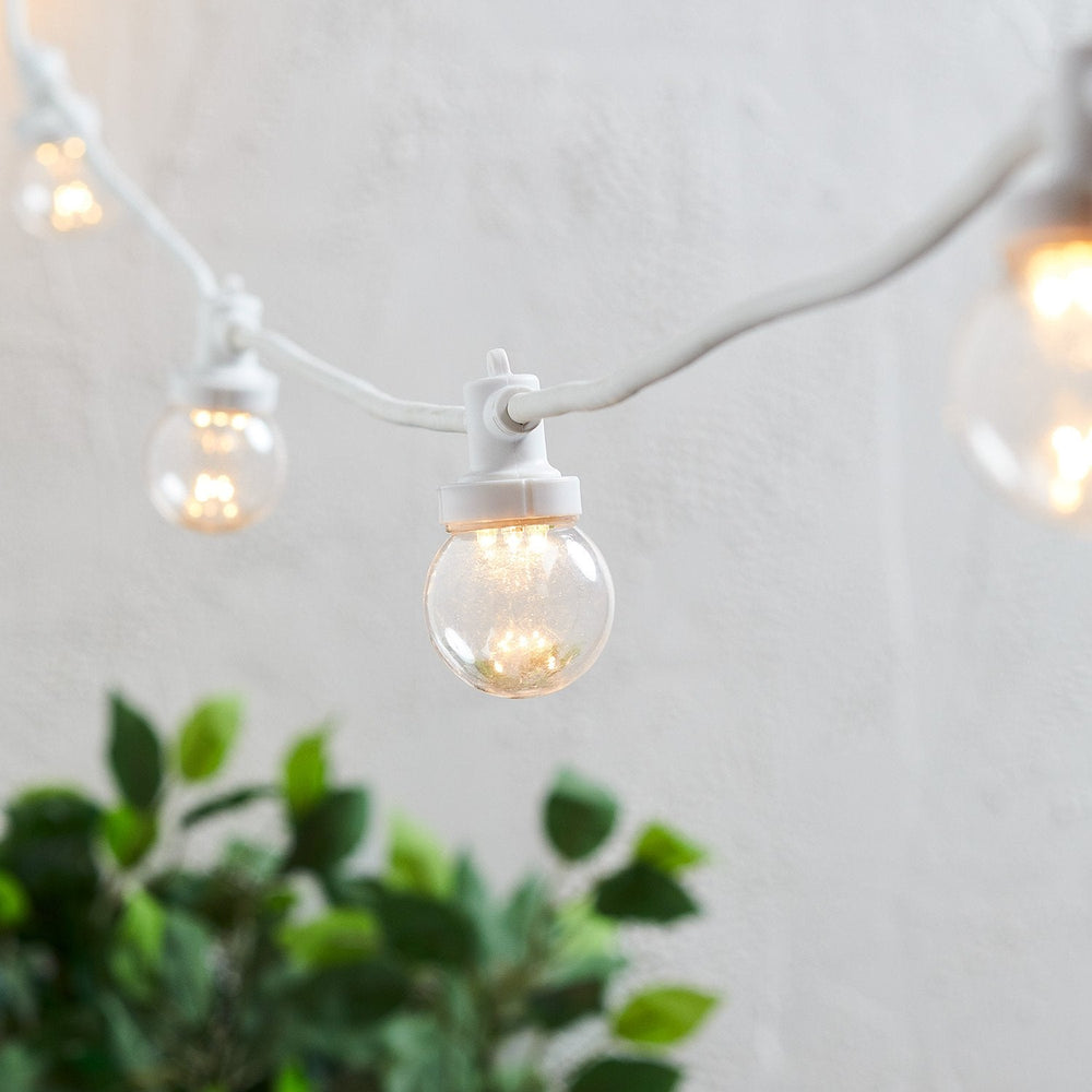 Warmweiße LED-Glühbirnen an weißem Kabel einer koppelbaren 20er Party-Lichterkette im Außenbereich