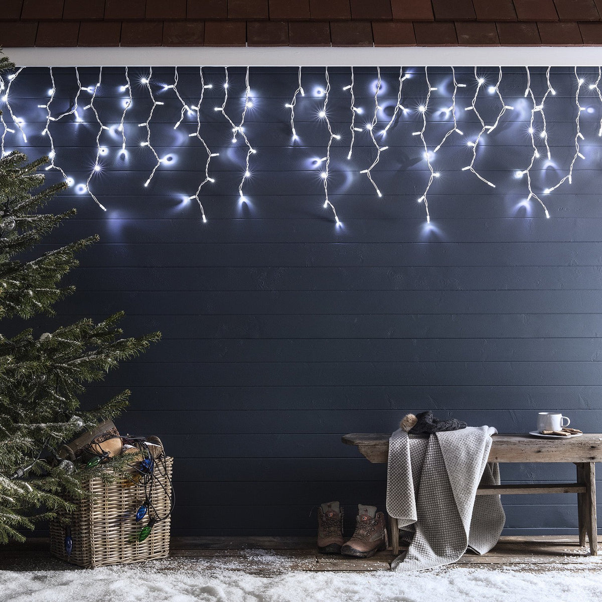 Lange weiße LED Eiszapfen-Lichterkette an dunkler Wand mit Winterdeko und Schnee
