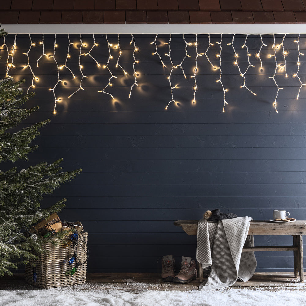 Lange LED Eiszapfen-Lichterkette an schwarzer Wand über Holzbänken mit Winterdeko