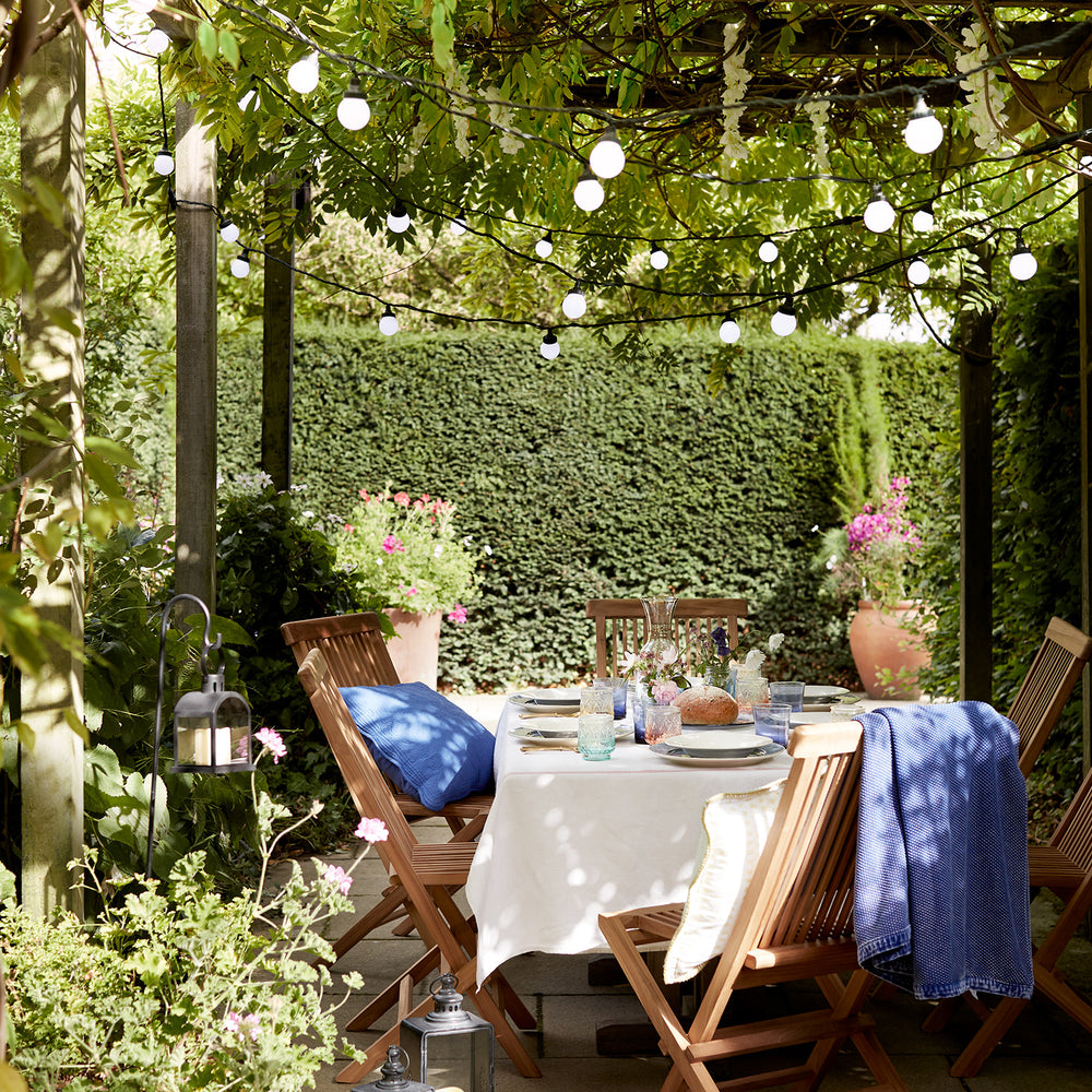 Pro Connect Lichterkette beleuchtet Pergola über gedecktem Gartentisch mit Holzstühlen