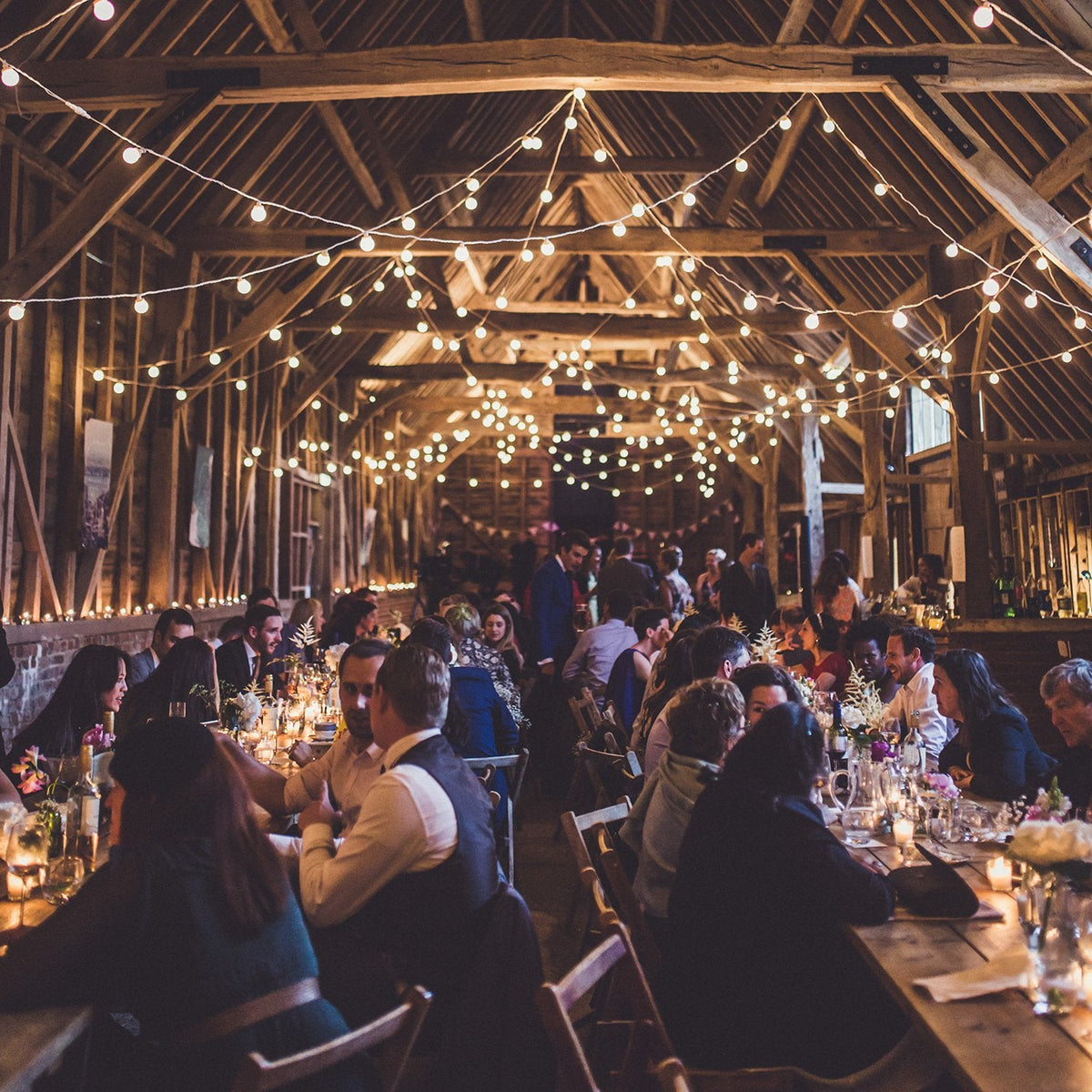 Rustikale Hochzeit mit vielen Gästen und warmweißen Lichterketten an Holzbalken