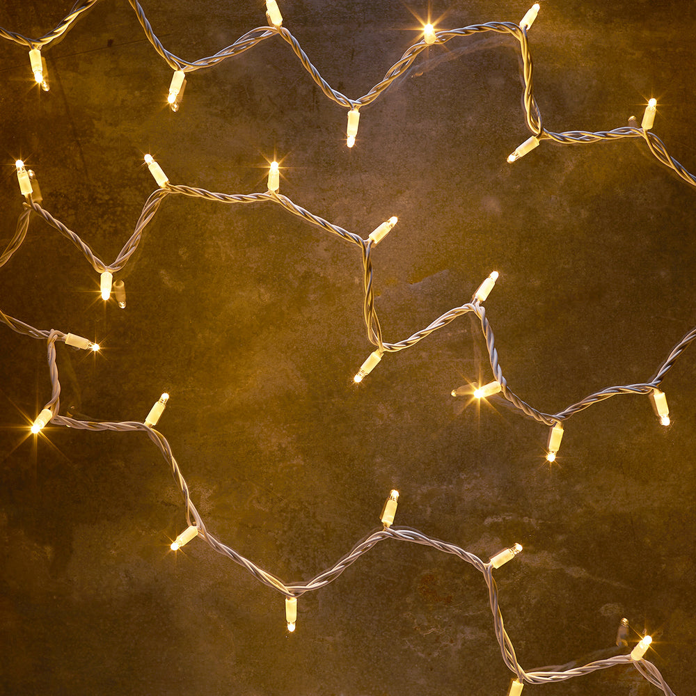 Warmweiße LED-Lichterkette mit 50 Lampen auf weißem Kabel, leuchtend auf dunklem Untergrund