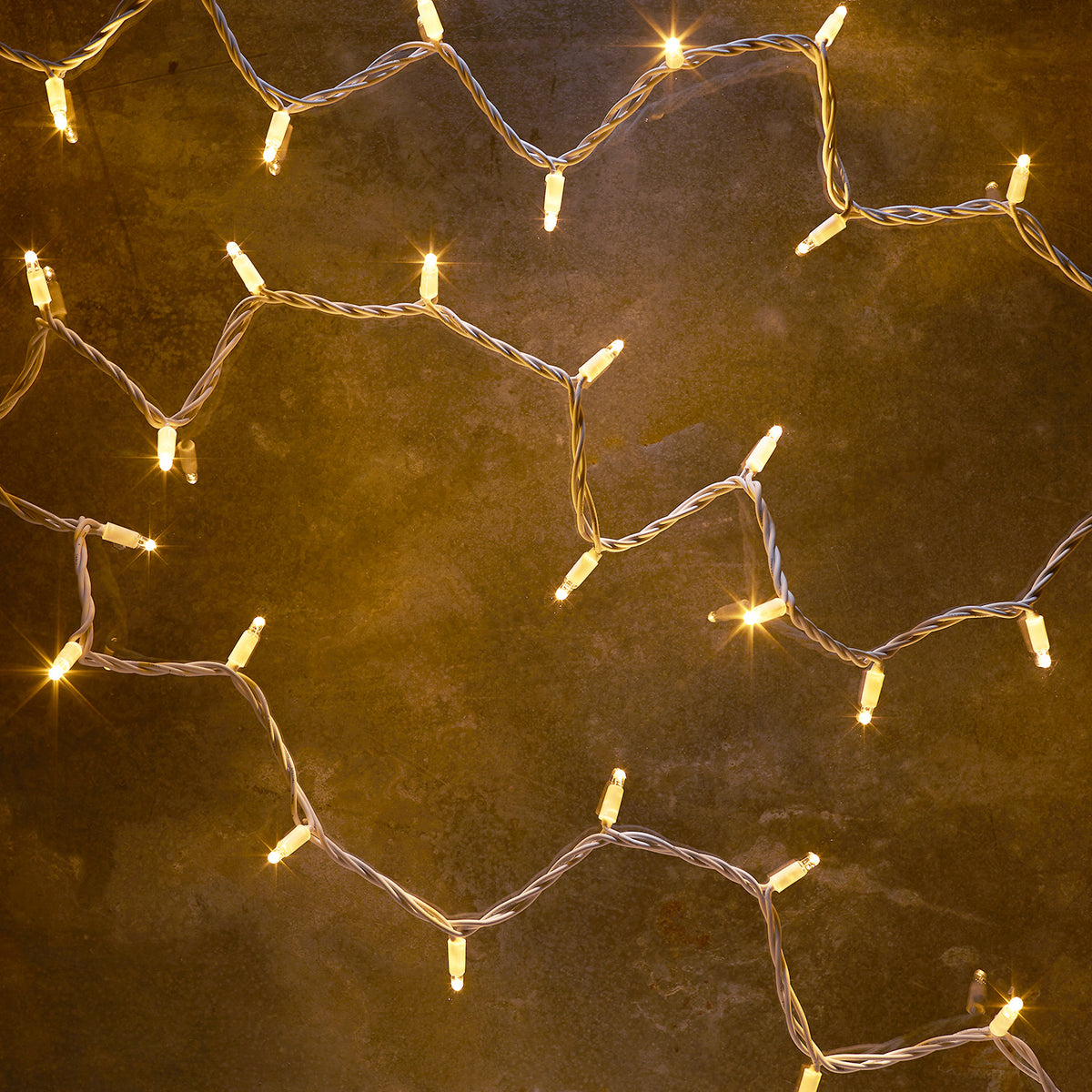 Warmweiße LED-Lichterkette mit 50 Lampen auf weißem Kabel, leuchtend auf dunklem Untergrund