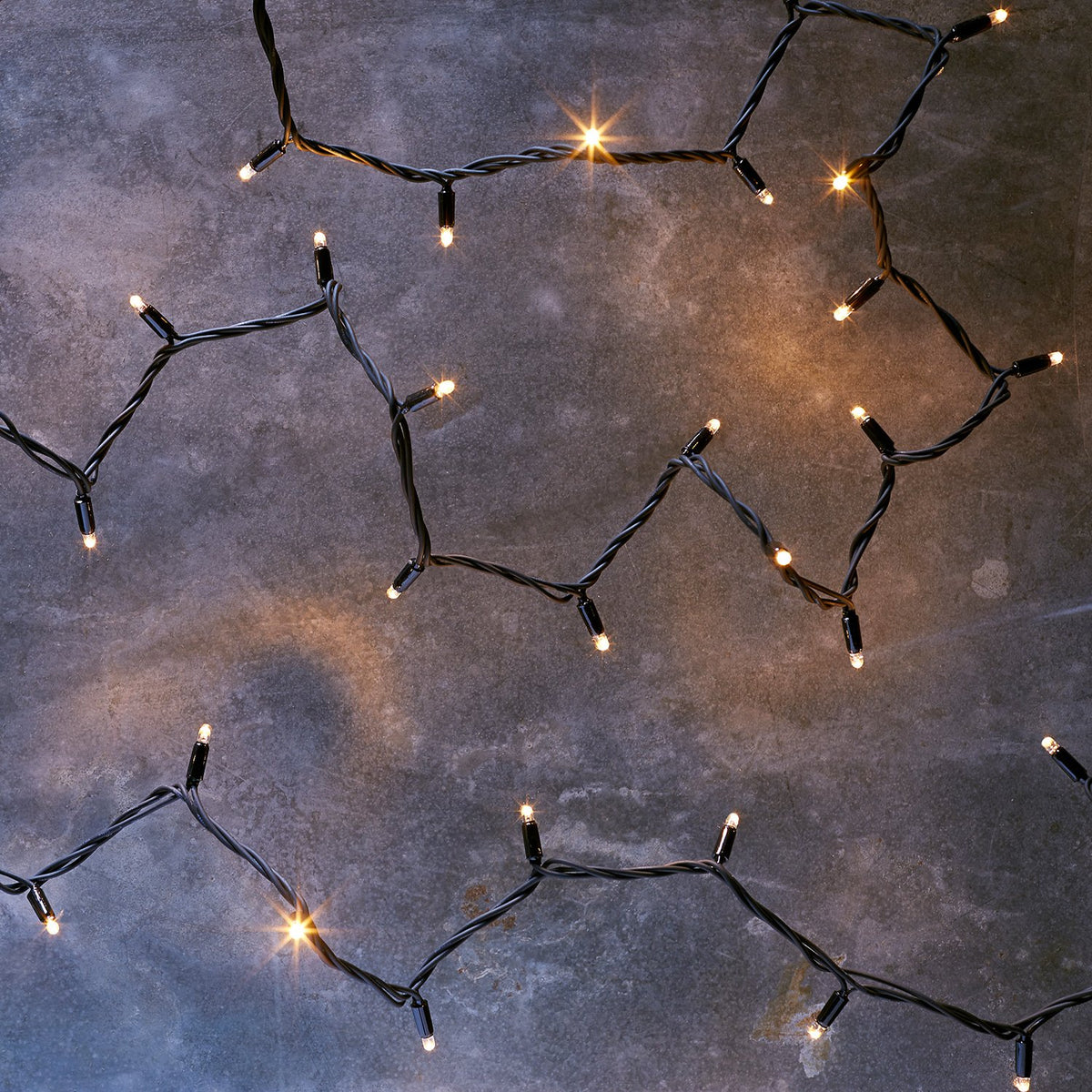 Nahaufnahme einer warmweißen LED Lichterkette mit schwarzem Kabel auf grauem Untergrund