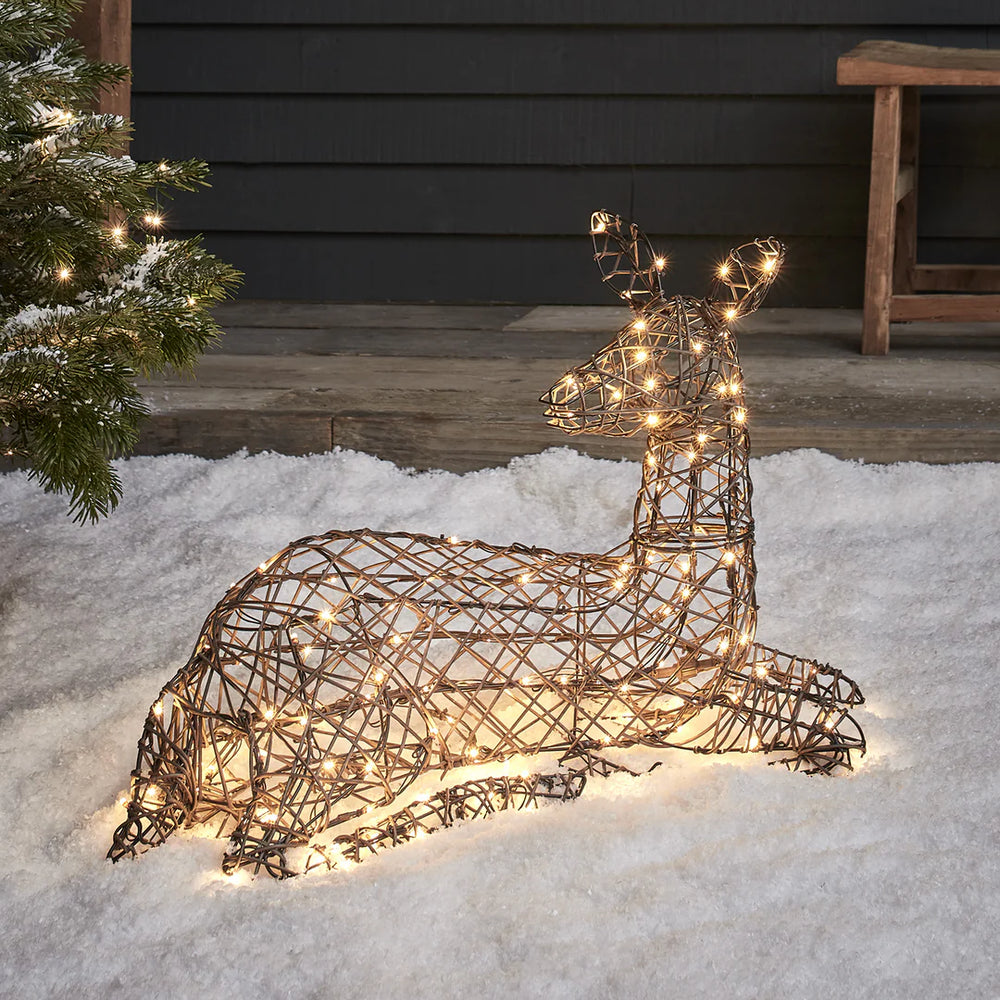 Liegendes LED-Rentier mit warmweißen LEDs auf Schnee vor einer Veranda mit Holzbank