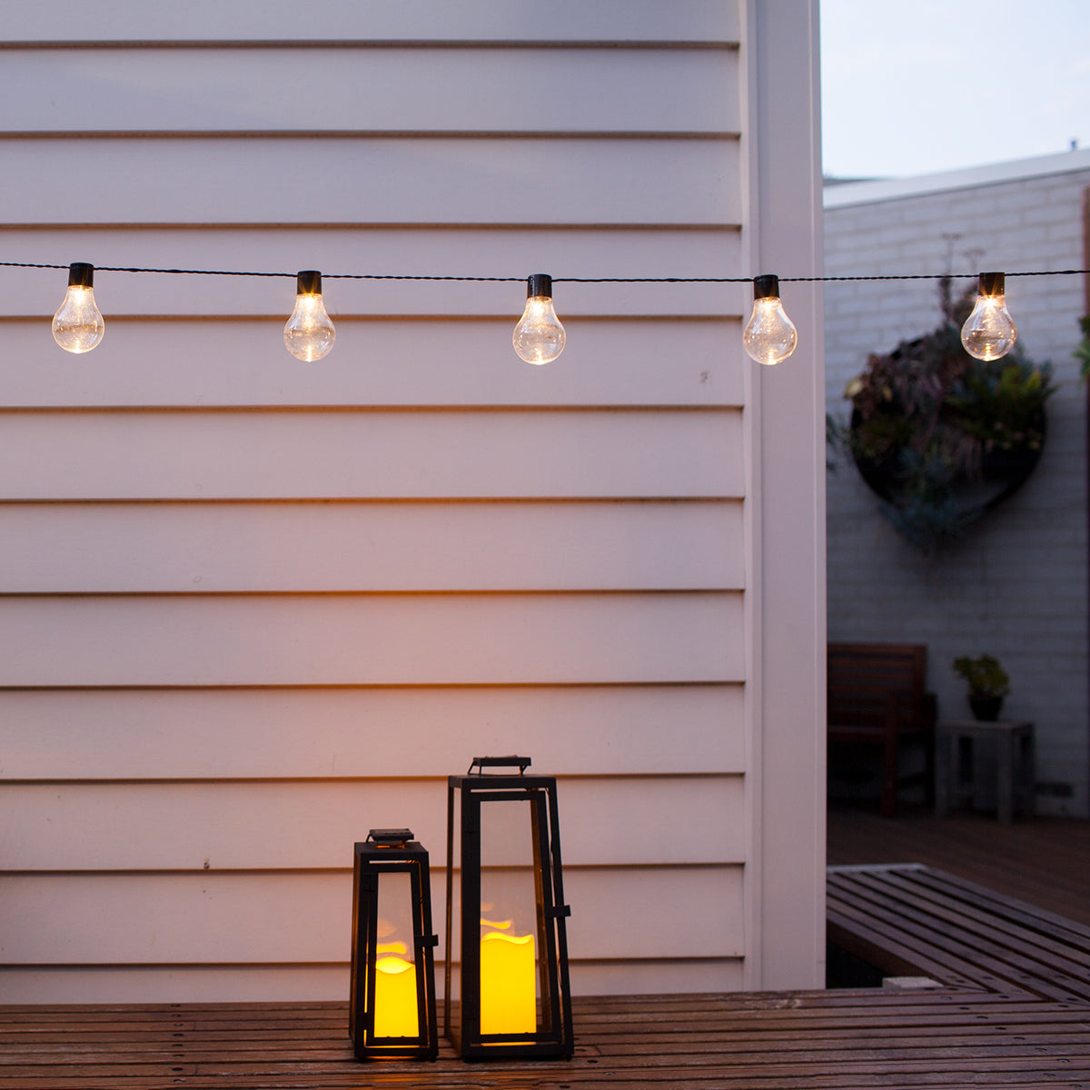 Solar Party Lichterkette mit warmweißen LEDs vor weißer Hauswand und drei leuchtenden Laternen
