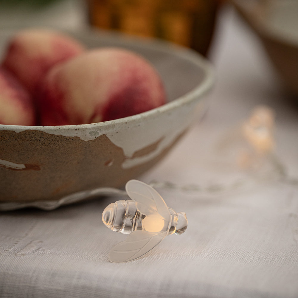 Solarbetriebene LED-Biene leuchtet warmweiß auf einem weißen Tuch neben einer Schale mit Pfirsichen