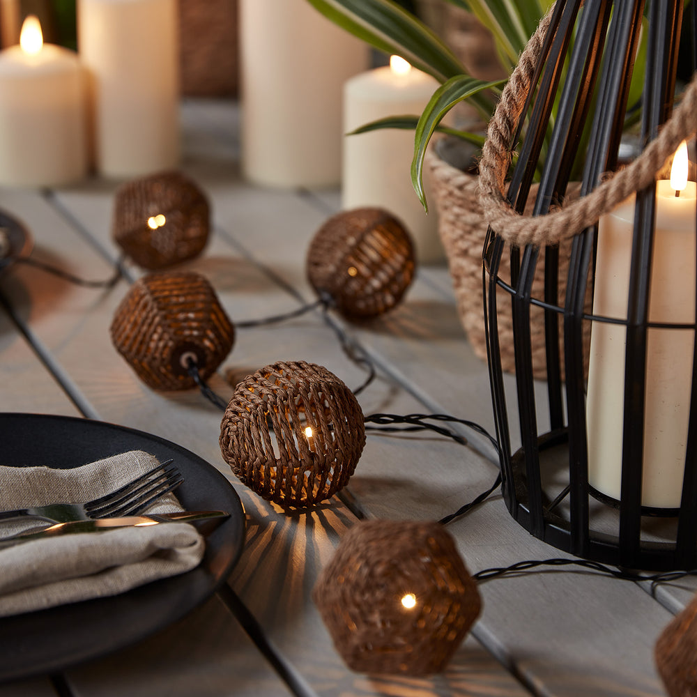 Solarbetriebene Lichterkette mit warmweißen LEDs in braunen Rattan-Kugeln auf einem Tisch mit Kerzen